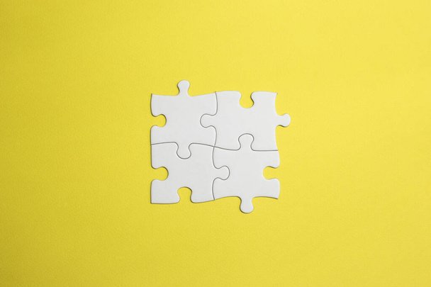 4 pièces d'un puzzle s'emboîtent pour former une équipe. pièces blanches pour faire une idée sous la forme d'un dessin, mot ou concept s'emboîtent. fond jaune - Photo, image