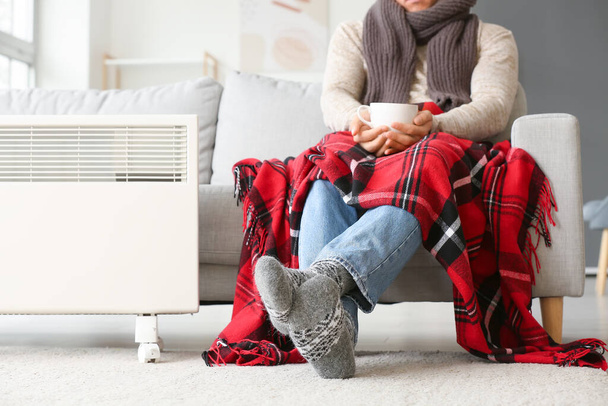 Νεαρός με ζεστά ρούχα και τσάι στο σπίτι. Έννοια της εποχής θέρμανσης - Φωτογραφία, εικόνα
