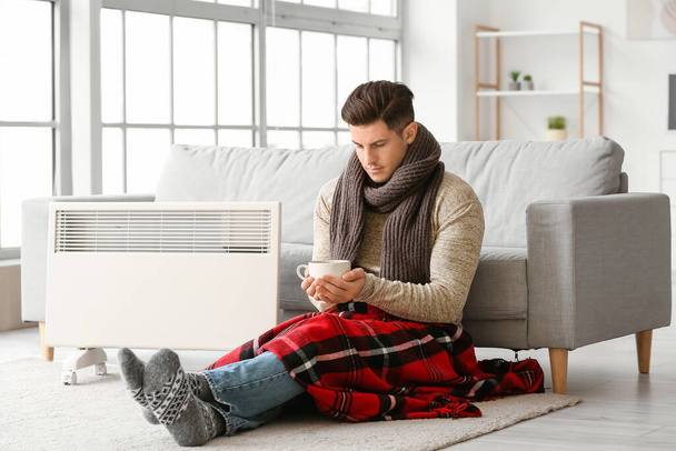 Young man in warm clothes and with cup of tea at home. Concept of heating season - Foto, Imagen
