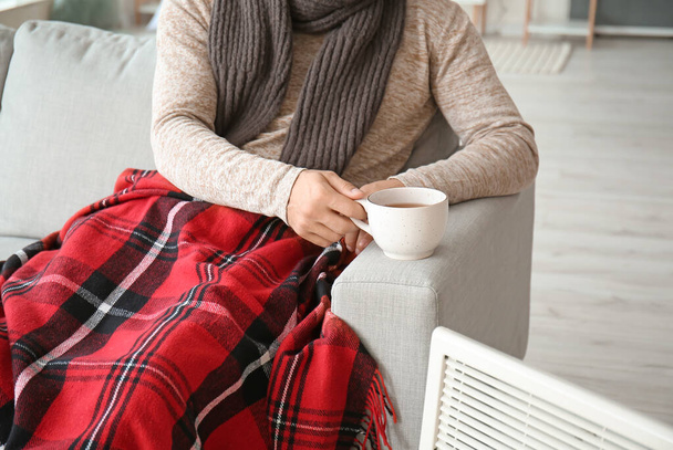 Young man in warm clothes and with cup of tea at home. Concept of heating season - 写真・画像