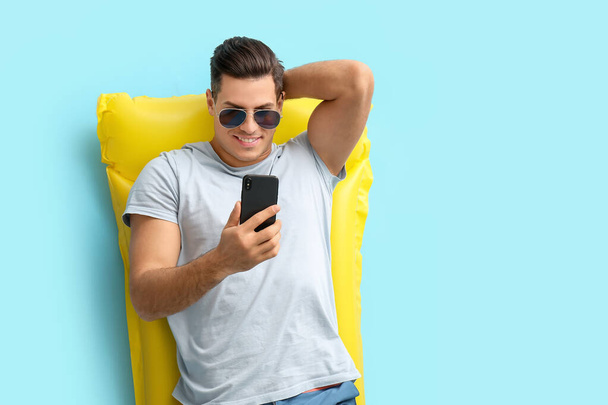 Young man with mobile phone lying on inflatable mattress against color background - Foto, Imagem