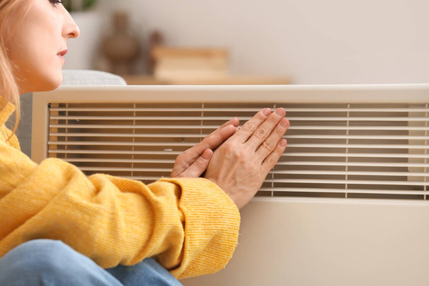 Felnőtt nő melegítő kezét mellett elektromos fűtőberendezés otthon. A fűtési idény fogalma - Fotó, kép