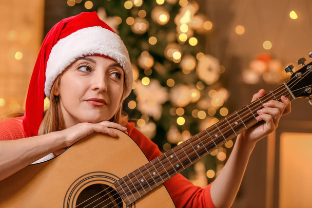 Зріла жінка грає на гітарі вдома напередодні Різдва
 - Фото, зображення