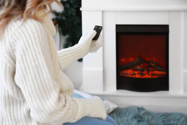 Young woman sitting near electric fireplace at home. Concept of heating season - Photo, Image