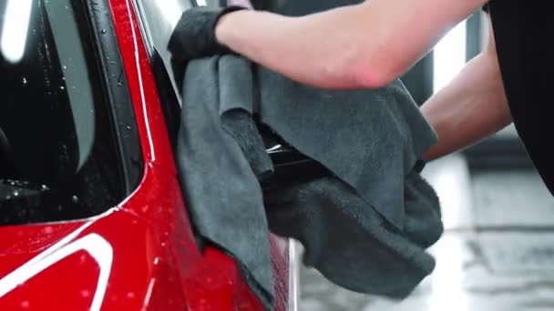 Servizio di lavaggio auto - l'uomo asciuga l'acqua da un'auto rossa con straccio - Filmati, video