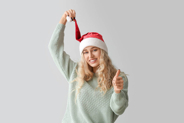 Belle jeune femme en chapeau de Père Noël montrant geste pouce vers le haut sur fond clair - Photo, image