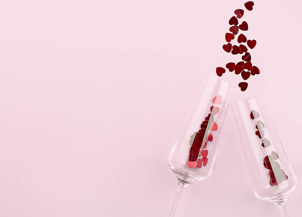 two wine glasses and confetti scattered in the form of hearts on a pink background - Photo, Image