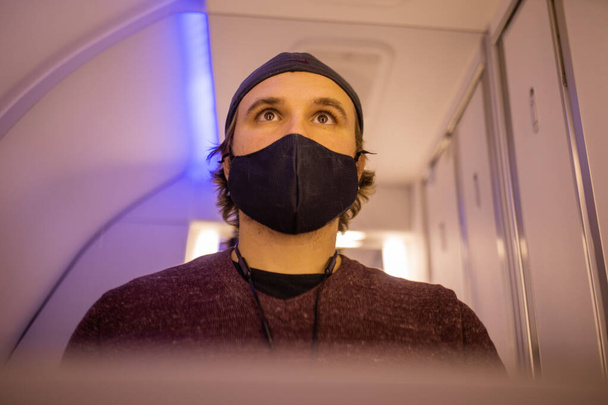 Zelfportret van een man met gezichtsmasker in de badkamer van het vliegtuig - Foto, afbeelding