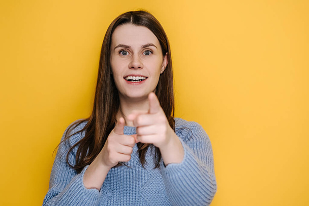Amazed funny millennial young girl pointing finger to camera, looking big eyes surprised expression, shocked by sudden success, wears sweater, isolated on yellow studio background. Wow, hey you! - Φωτογραφία, εικόνα