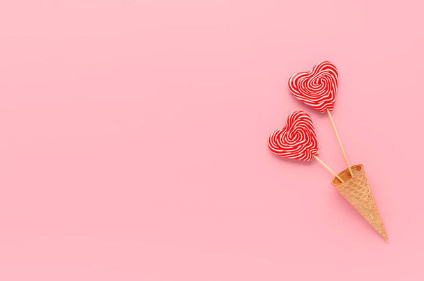 Two heart lollipops in waffle cone on pastel pink background. Minimal composition, Flat lay, top view, empty space. Valentine's day greeting card - Fotoğraf, Görsel