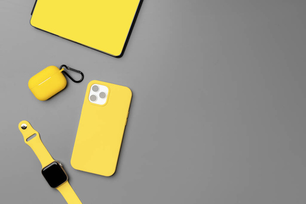 Yellow notepad with smartphone, smartwatch and earphones on gray background - Фото, изображение
