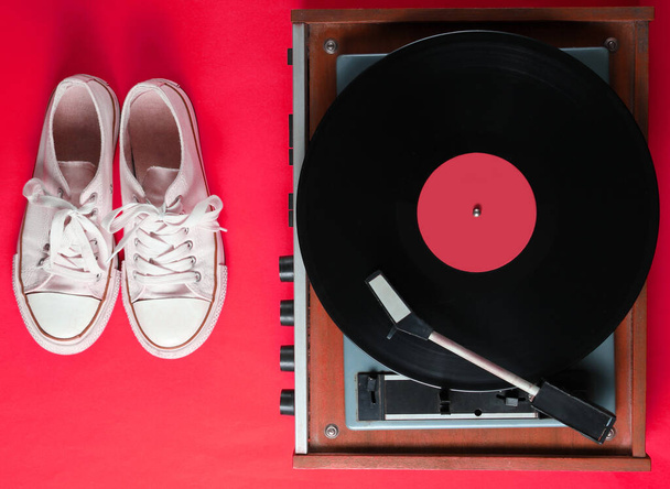 Vinylspieler, alte Turnschuhe auf rotem Hintergrund. Retro-Stil, Popkultur, 80er Jahre, Draufsicht - Foto, Bild
