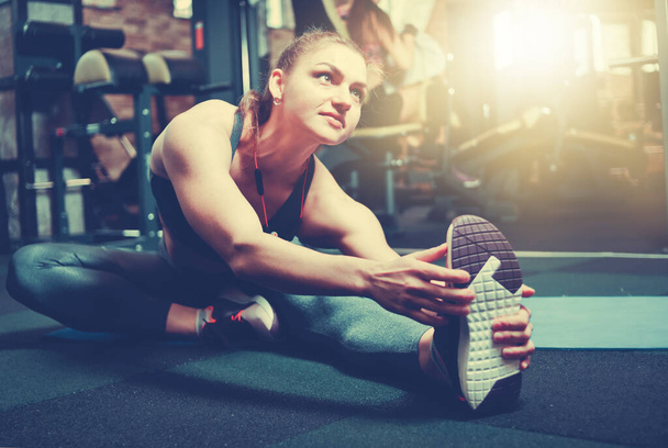 Young sporty woman stretching her right leg in gym - Photo, image