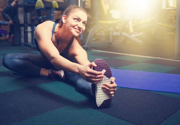 Young sporty woman stretching her right leg in gym - Photo, Image