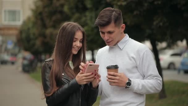 Una mujer joven está mostrando fotos en un teléfono inteligente a un hombre. Se ríen y beben café. 4K - Metraje, vídeo