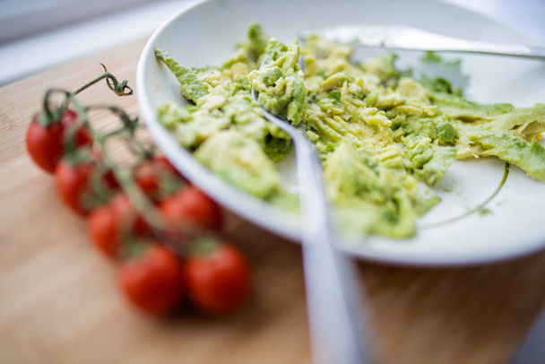 Cherry tomatoes and bowl of mashed avocado on wooden table - Photo, Image