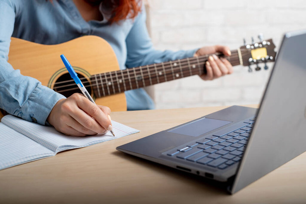 A woman with a guitar writes notes in a notebook. The girl composes a song - Photo, Image