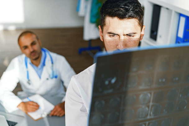 Two male doctors examine MRI brain scan of a patient in cabinet - Foto, Imagen