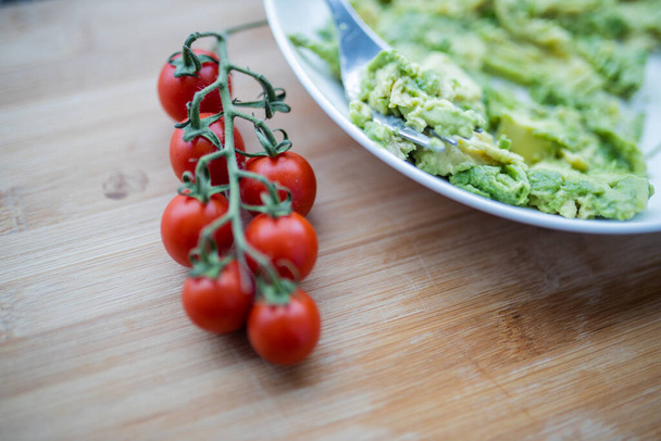 Cherry tomatoes and bowl of mashed avocado on wooden table - Photo, Image