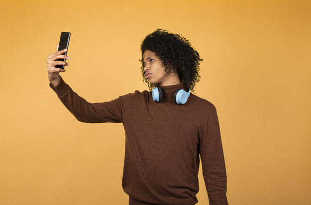 Imagem do jovem afro-americano posando isolado sobre fundo amarelo tirando uma selfie com o telefone. - Foto, Imagem
