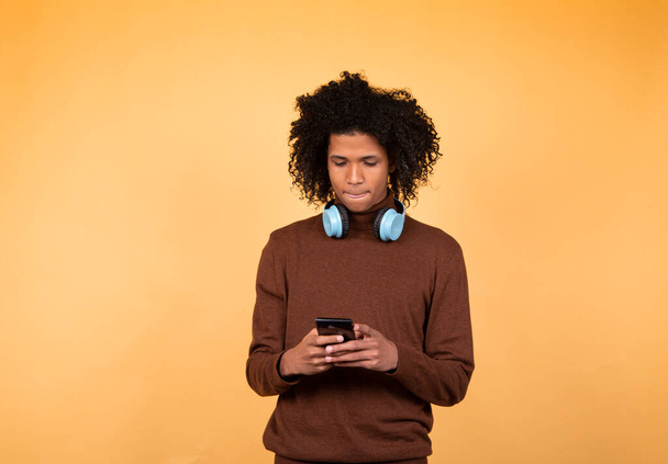 Guy with afro hair, writes text messages on cell phone, enjoys online communication, writes comments isolated on yellow studio wall. Technology concept - Fotó, kép