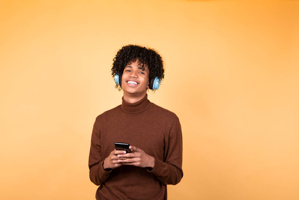Young afro hair man standing in poses isolated on yellow background using mobile phone device, writes text messages on modern smartphone, watches funny videos during free time - Foto, immagini