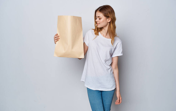 Μια γυναίκα με λευκό μπλουζάκι και τζιν με ένα πακέτο στα χέρια της με ψώνια. - Φωτογραφία, εικόνα