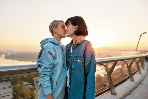 Mladé vášnivé lesbičky pár líbání venku, dvě ženy těší romantické chvíle spolu při východu slunce - Fotografie, Obrázek