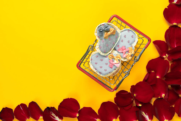 plat gelegd, verschillende stoffen hartjes liggen in een mandje op een oranje achtergrond bij rozenblaadjes. Concept om Valentijnsdag te vieren. Kopieerruimte. - Foto, afbeelding