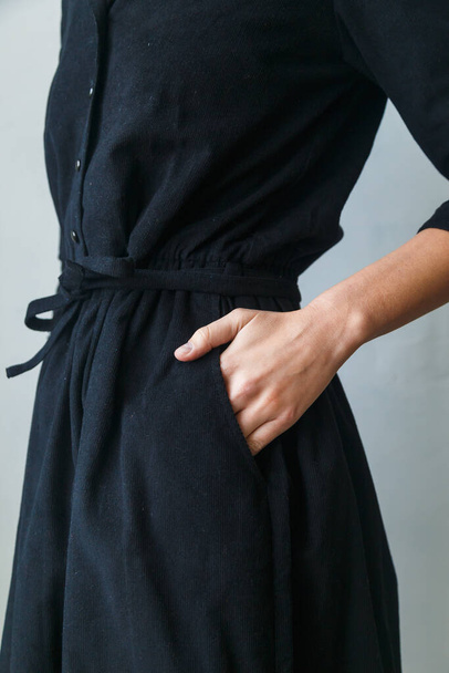 wunderschönes schwarzes Cordkleid auf einem Mädchen in Nahaufnahme. Hand am Gürtel - Foto, Bild