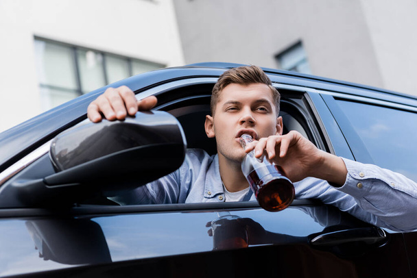 пьяный мужчина пьет алкоголь, глядя в окно машины - Фото, изображение
