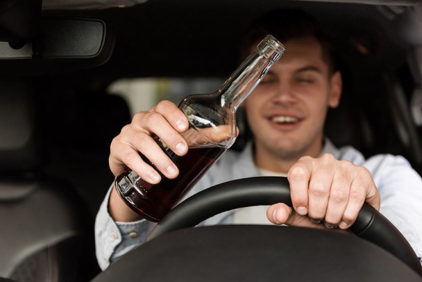 borracho con botella de whisky conduciendo coche sobre fondo borroso - Foto, Imagen