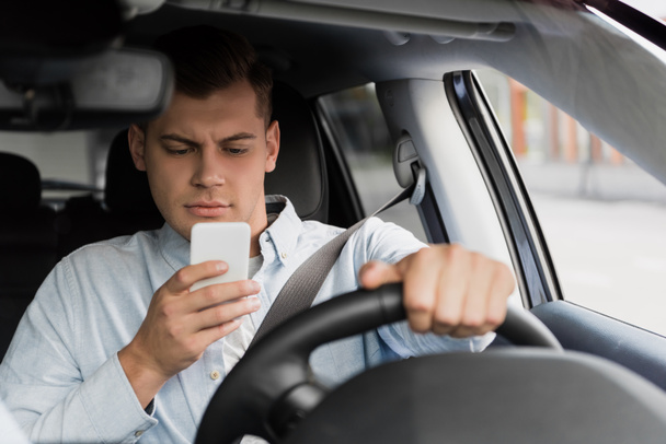 mladý muž chatování na smartphone při řízení auta, rozmazané popředí - Fotografie, Obrázek