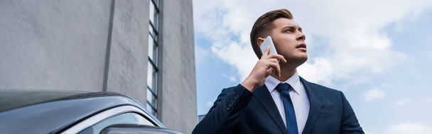 young businessman looking away while talking on smartphone outdoors, banner - Photo, Image