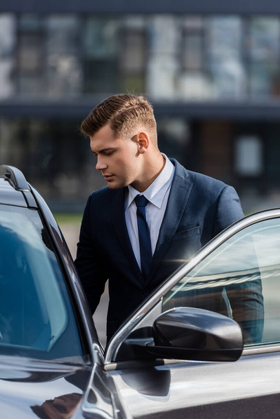 Young businessman standing near auto with open door outdoors - Foto, Imagem