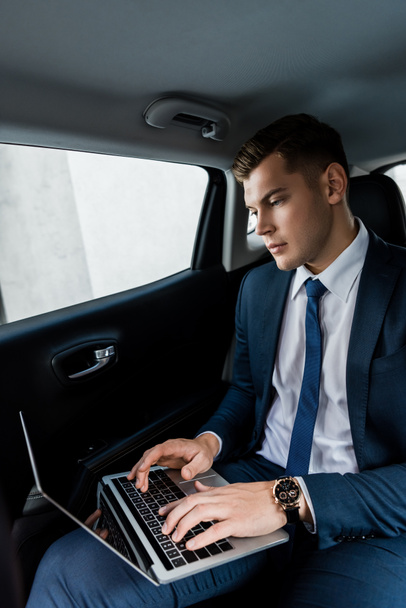 Uomo d'affari in abbigliamento formale utilizzando il computer portatile sul sedile posteriore della macchina - Foto, immagini