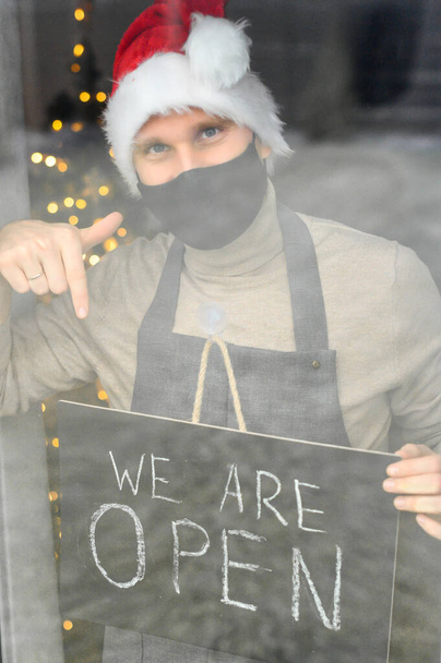 Young man in mask holding open sign in cafe - Foto, Bild