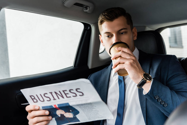 Empresario bebiendo café para llevar y leyendo periódico en coche - Foto, Imagen