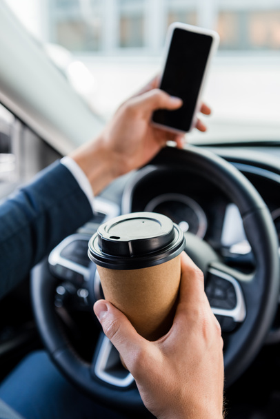 Cropped view of businessman holding coffee to go and smartphone on blurred background in car - Fotografie, Obrázek
