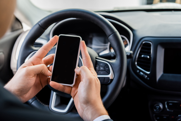 Widok człowieka trzymającego smartfona z pustym ekranem w pobliżu kierownicy w samochodzie na rozmytym tle - Zdjęcie, obraz