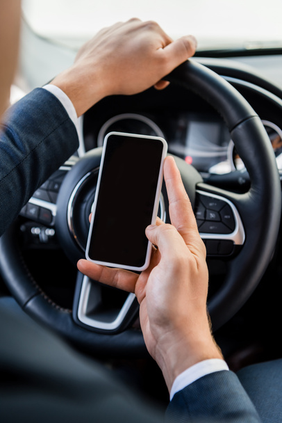 Cropped view of businessman holding smartphone with blank screen while driving car on blurred background - Photo, Image