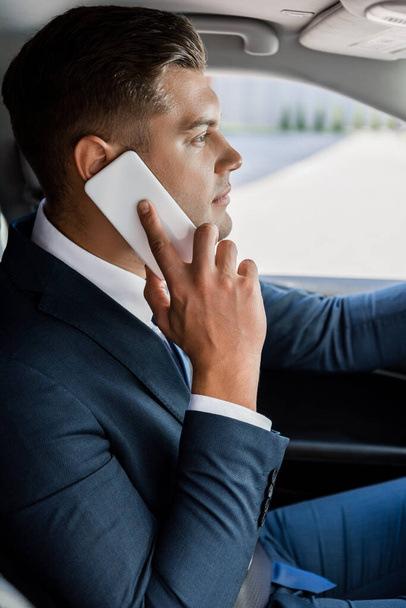 Молодий бізнесмен розмовляє на смартфоні в авто на розмитому фоні
 - Фото, зображення