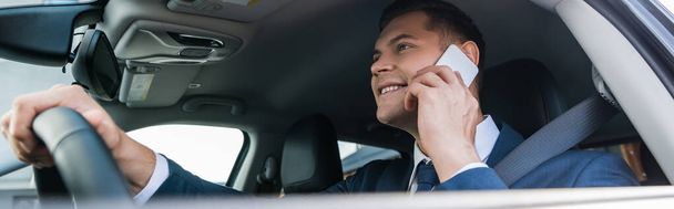 Hombre de negocios positivo hablando por teléfono celular mientras conduce auto en primer plano borroso, banner - Foto, Imagen