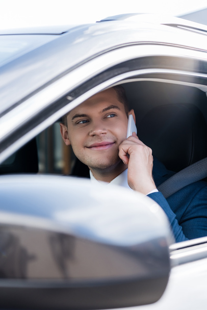 Smiling businessman talking on smartphone in auto on blurred foreground - Photo, Image