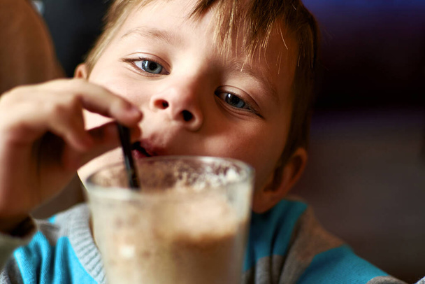 Little boy drinks a cocktail from a straw in a cafe. - Foto, Imagem