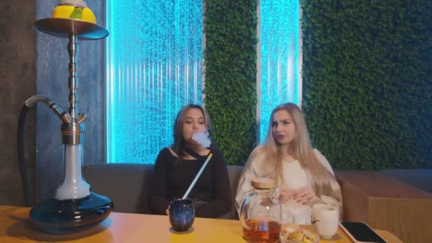 Két női barát a vízipipa bárban. Az egyik nő dohányzik, a másik visszautasítja és teát iszik. - Felvétel, videó