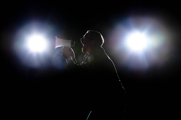 Силуэт человека с мегафоном изолирован на темном фоне при свете фонарей - Фото, изображение