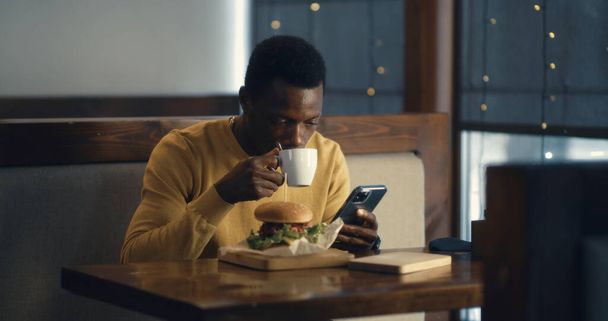 Black guy having meal in cafe after pandemic and using phone - Photo, Image