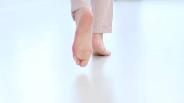 defocus, Side close up view of unrecognizable woman feet legs, barefoot girl standing indoors inside of modern home enjoy warm wooden heated floor. soft focus - 写真・画像