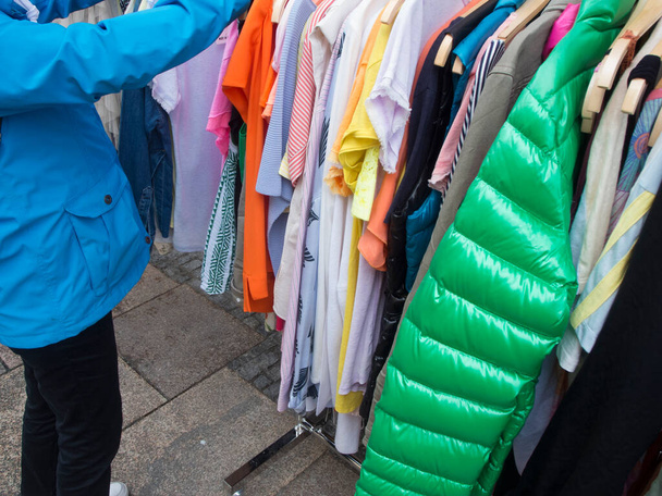 Различные блузки и куртки на стойке возле магазина одежды с неузнаваемым человеком в синем. - Фото, изображение